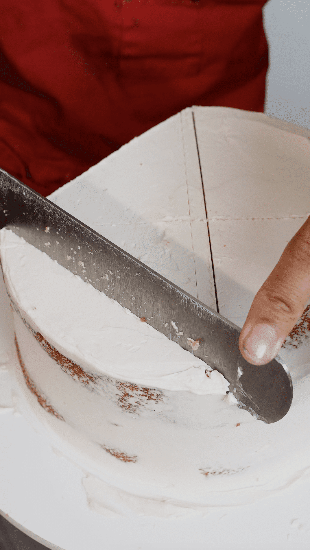 Baker using a serrated knife to cut away side sections of the layer to create the curved top edges.